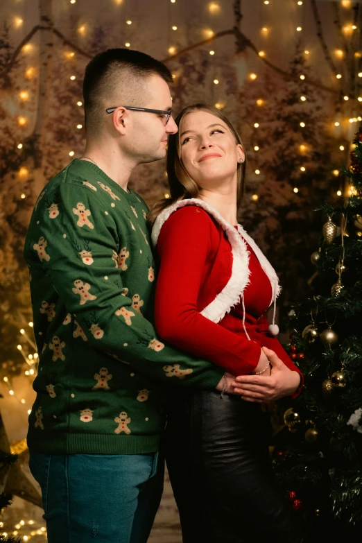 a beautiful couple pose for a christmas picture with their light up trees in the background