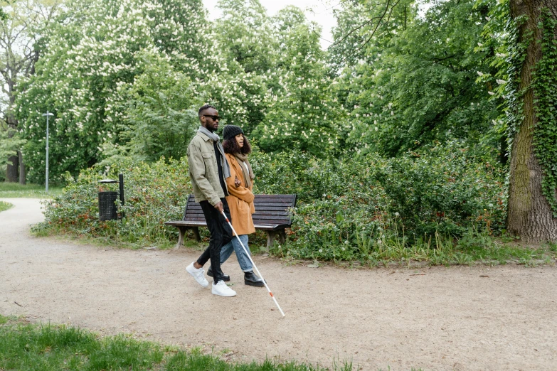 a man and a woman walking through the park with sticks