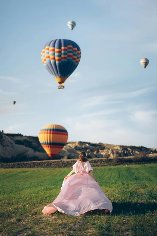 a woman is looking up at several  air balloons in the sky