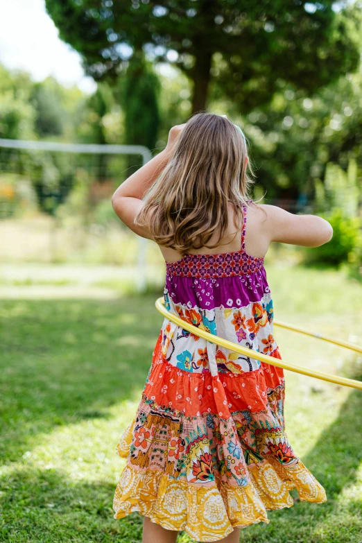 the little girl in the colorful dress is holding onto an orange ring