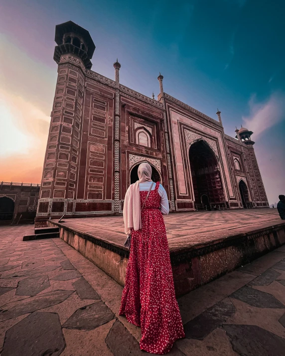 a women in an islamic gown stands in front of a massive building