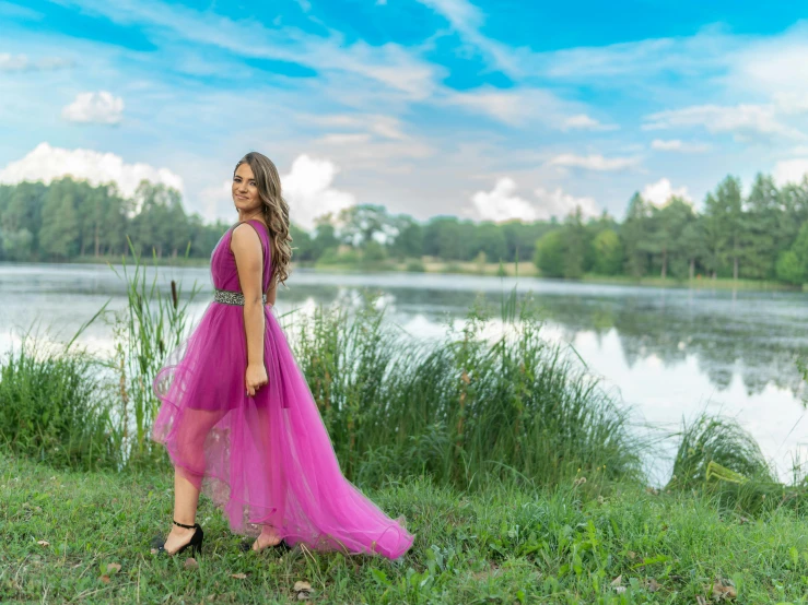 a woman in a pink dress standing in grass next to the water