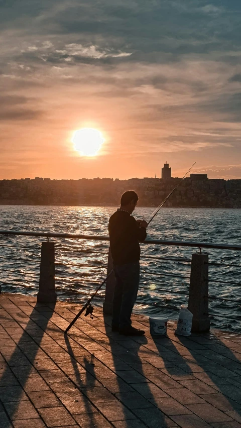 a man is fishing on a pier at sunset