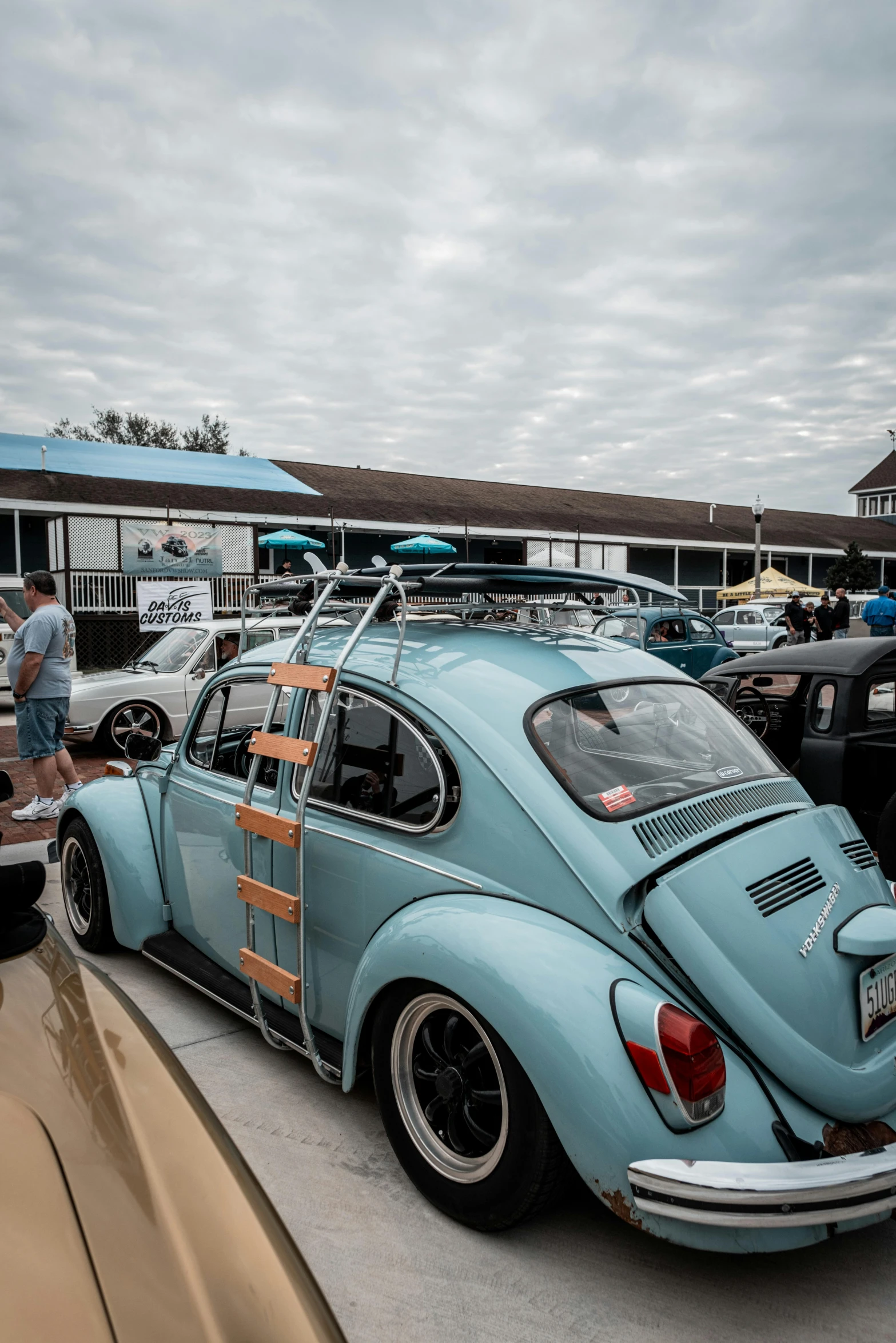 an old blue beetle is parked outside near people