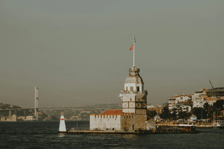 a tall lighthouse on the water near a bridge