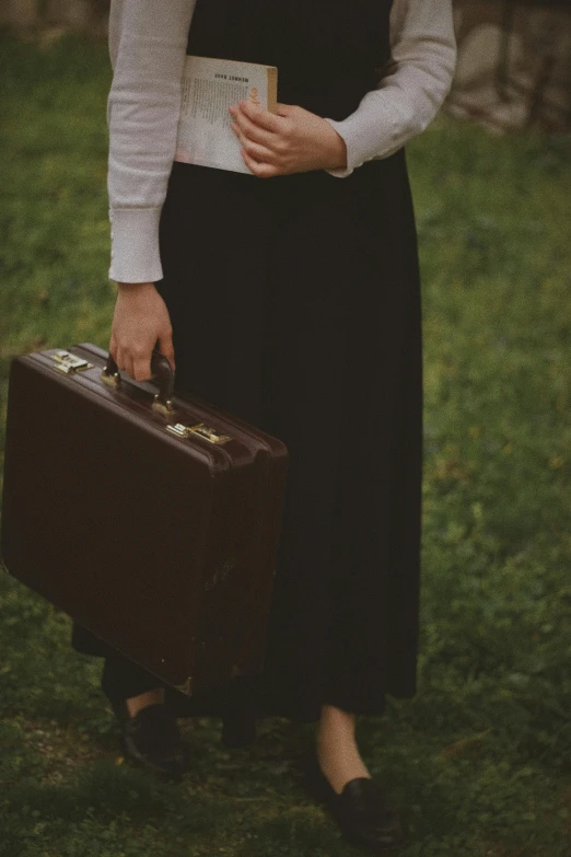 a woman holding a brown suitcase standing on a field