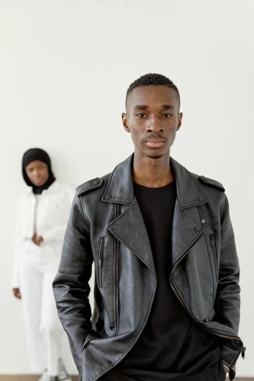 man in leather jacket looking at camera while woman stands nearby