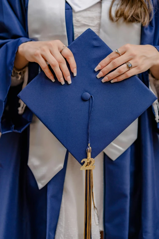 a female graduate stands in a gown and holds her tassel