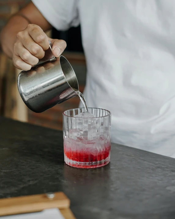 bartender mixing liquid from metal pitcher to cup for small serving