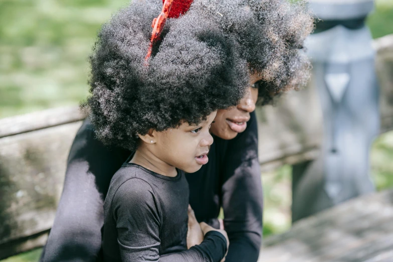 an adorable little girl sitting on a bench with an afro