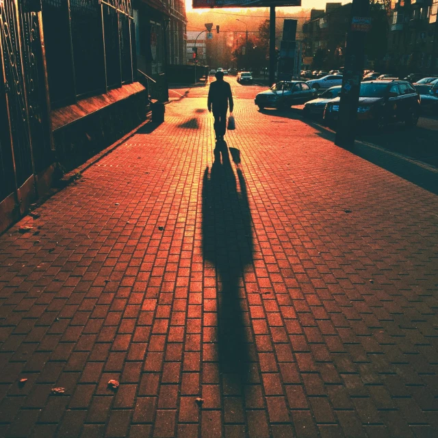 person walking down a brick sidewalk in a town with cars