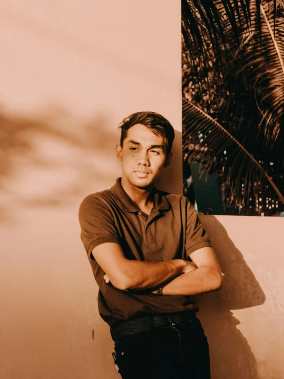 a man in brown shirt leaning against a wall