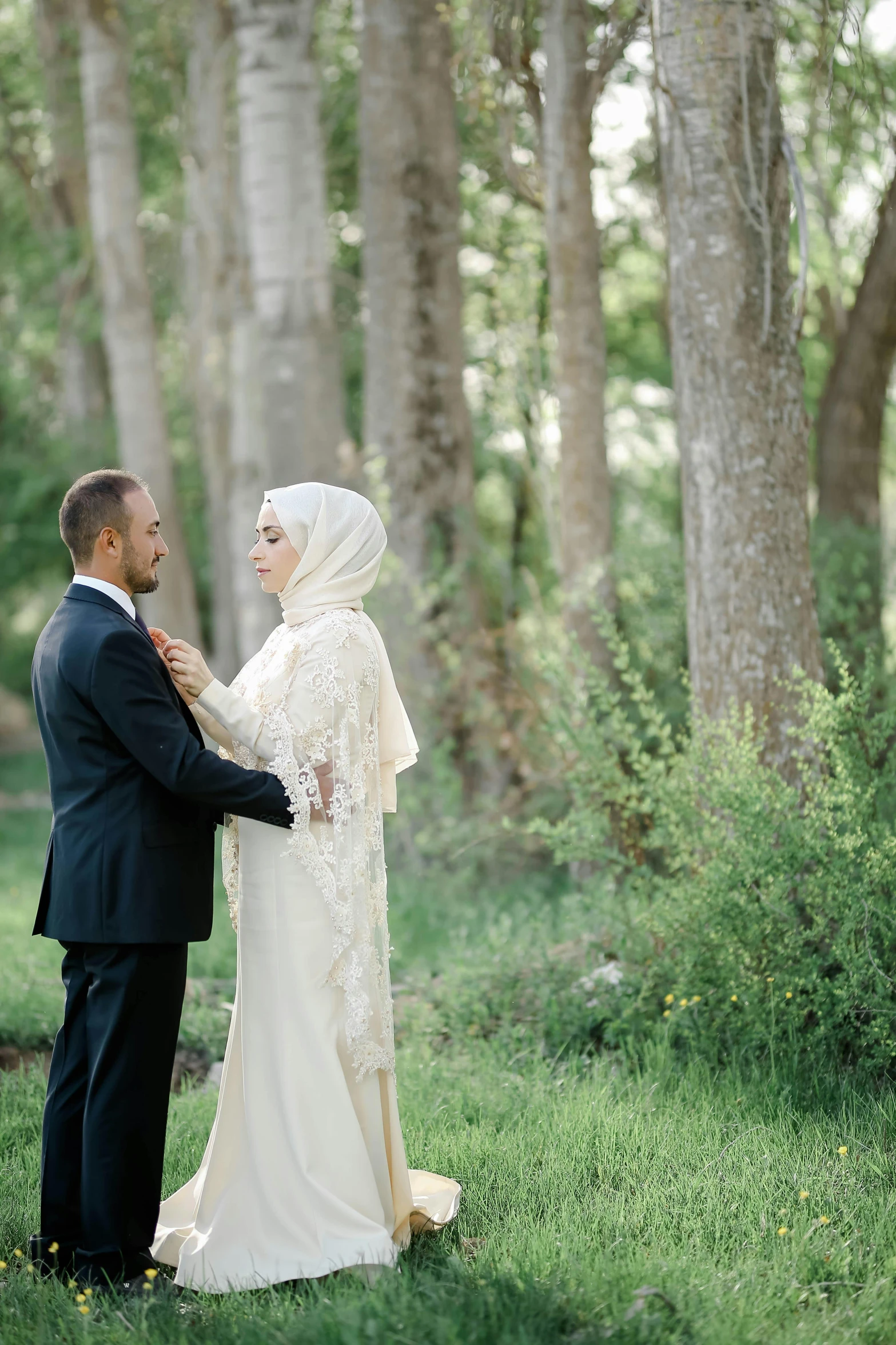 a bride in an islamic garb and groom in black tuxedo pose for their wedding po in a forest