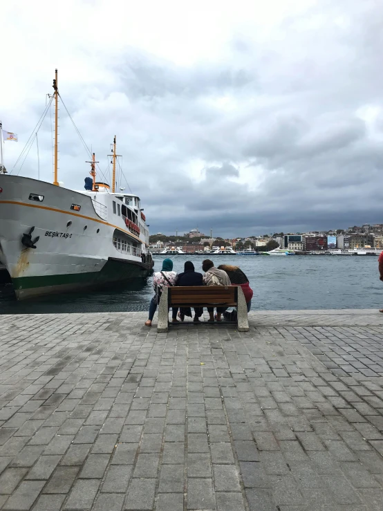 several people stand at a park with a boat on the water