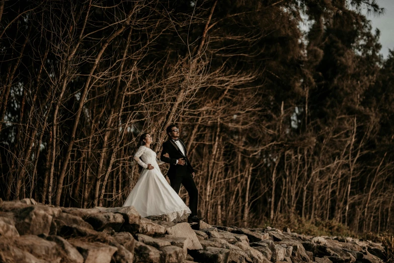 a bride and groom are standing on rocks by the woods