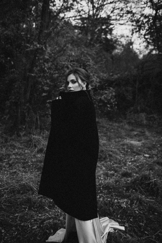 woman in black standing near a forest with her hands on her hip