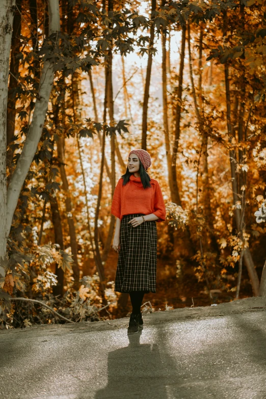 a girl is walking in the forest with an orange sweater