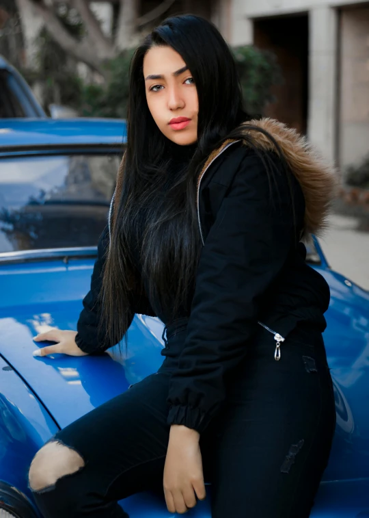 a woman leaning on the hood of a blue car
