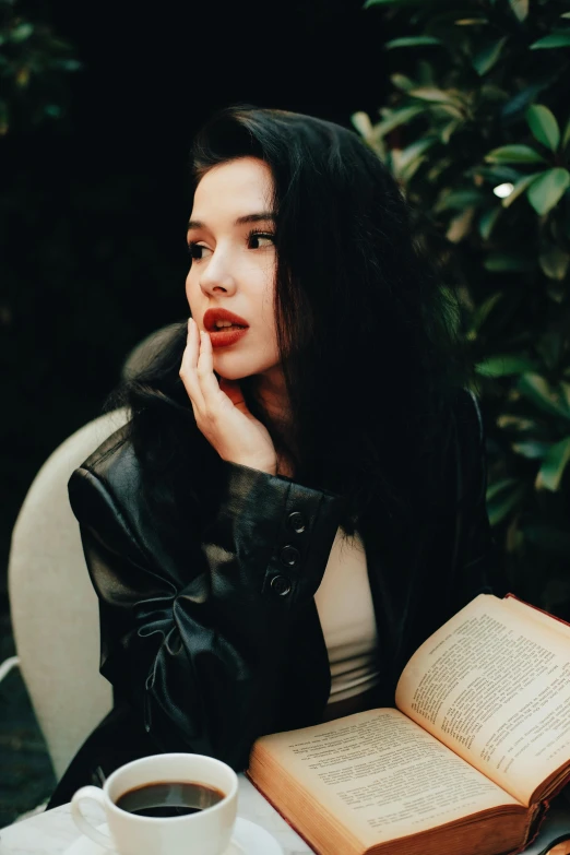 a beautiful woman sitting in front of an open book with a cup of coffee