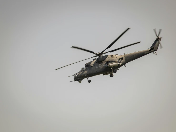 a military helicopter flying through a gray sky