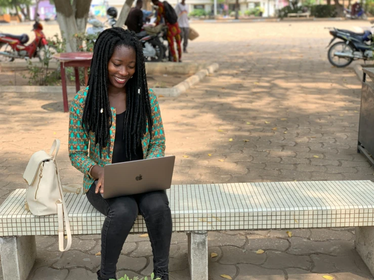 a black woman sitting on a park bench using her laptop