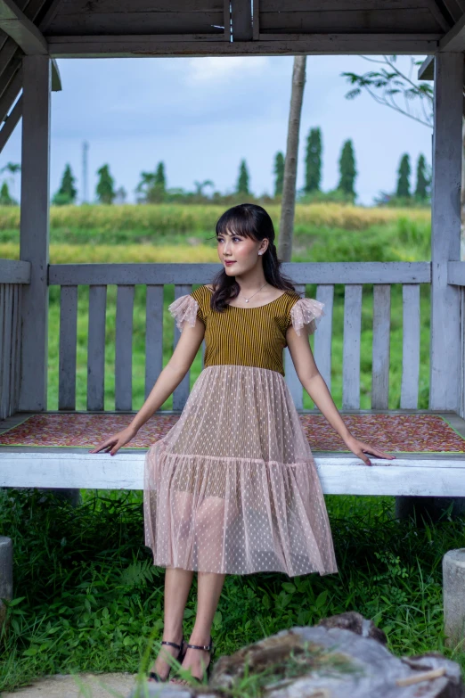 a  wearing a pink dress stands on a wooden bench in front of some trees