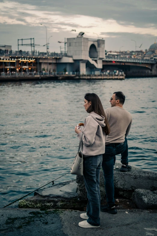 two people standing on a rock near the water and looking at soing