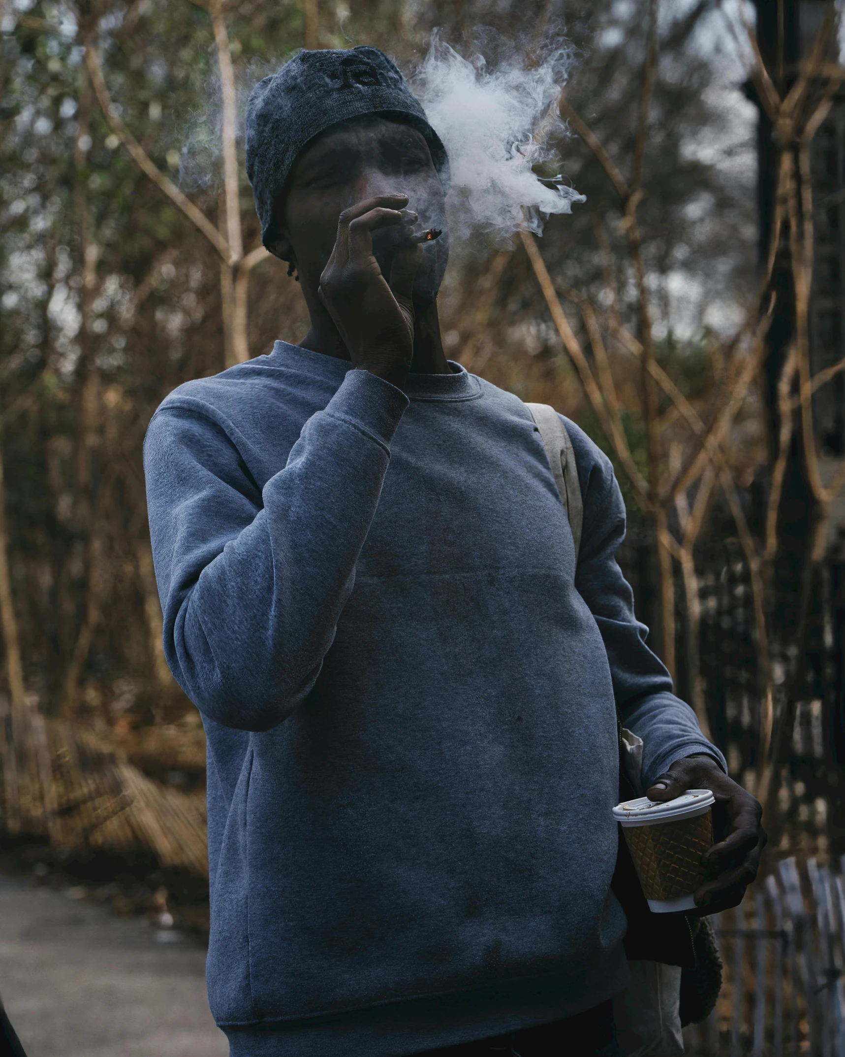 a man in a blue sweater smokes an electronic cigarette