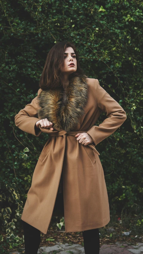 a woman stands in a wooded area wearing a coat with gold beads