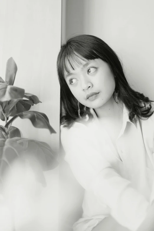 a girl poses next to a plant while holding her hand under the face