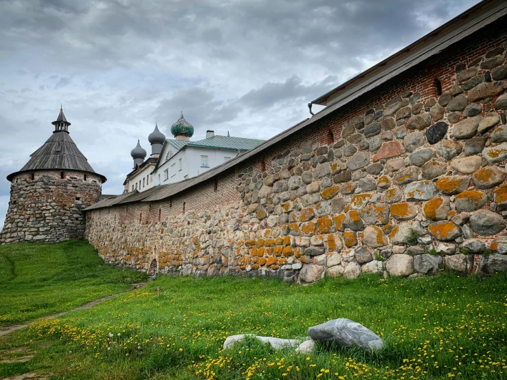 a stone wall with two green spires on top and yellow flowers in the grass next to it