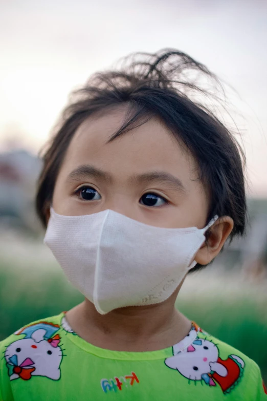a child wears a white mask while wearing a green shirt