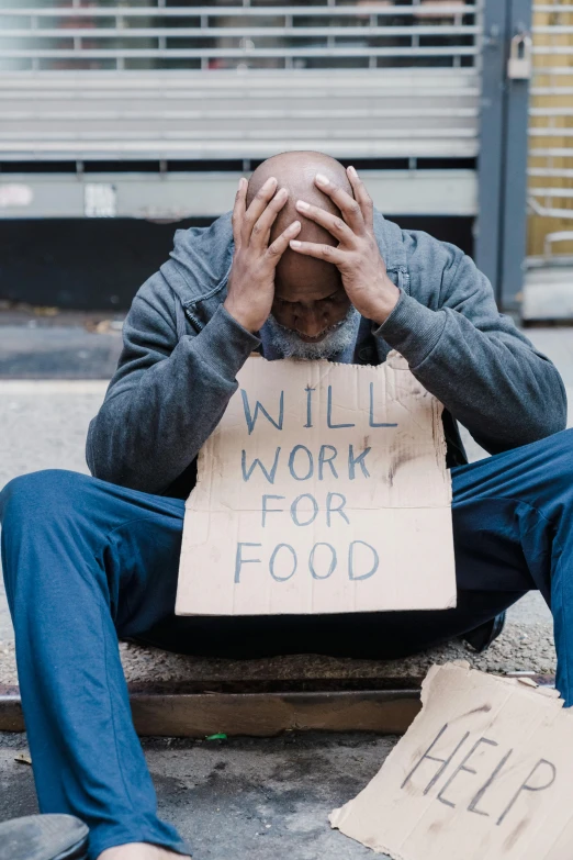 a homeless man sitting on the street and holding a sign that reads will work for food