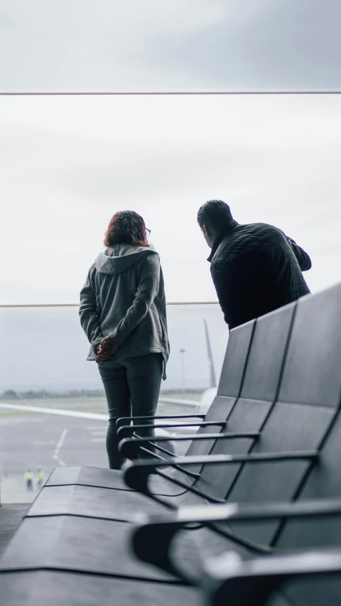 two people stand next to luggage at an airport