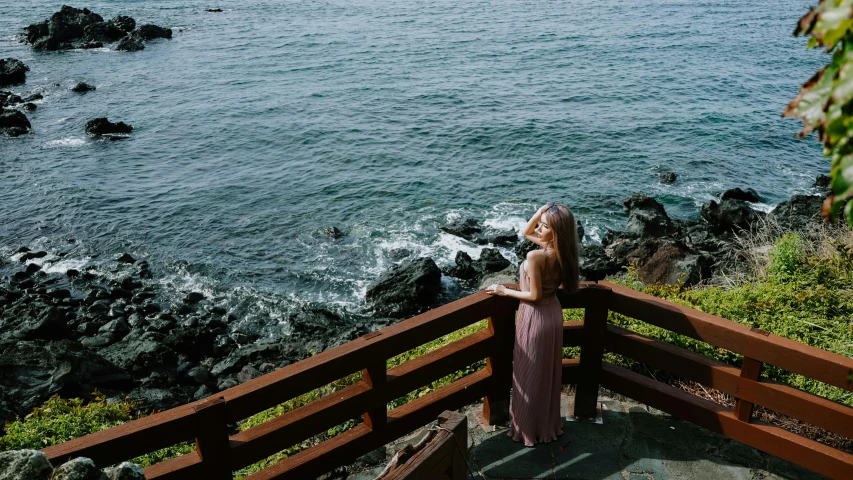 a beautiful young woman standing on top of a railing next to the ocean