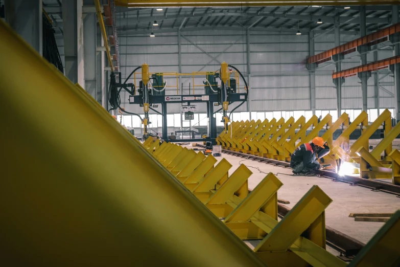 workers work inside a factory building with yellow beams