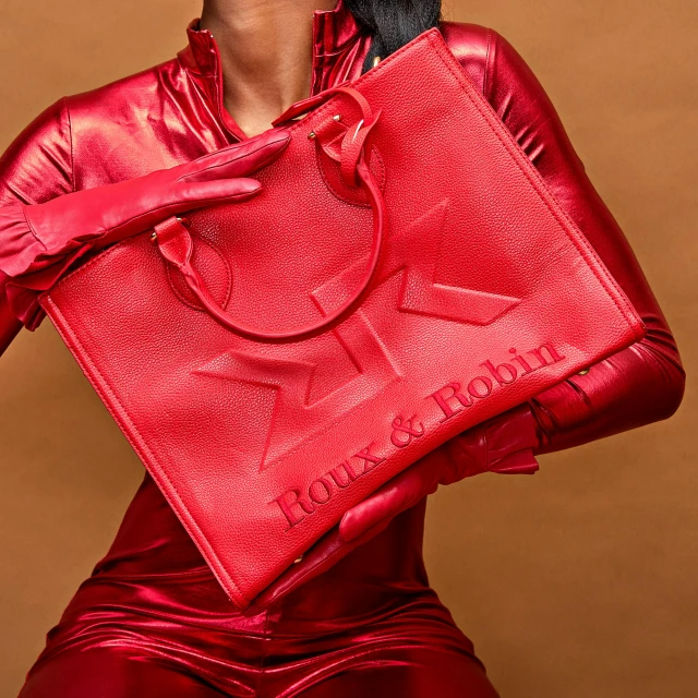 the back view of a model wearing a red dress and carrying a large bag