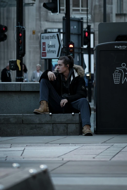 a man sits on a bench near a garbage can