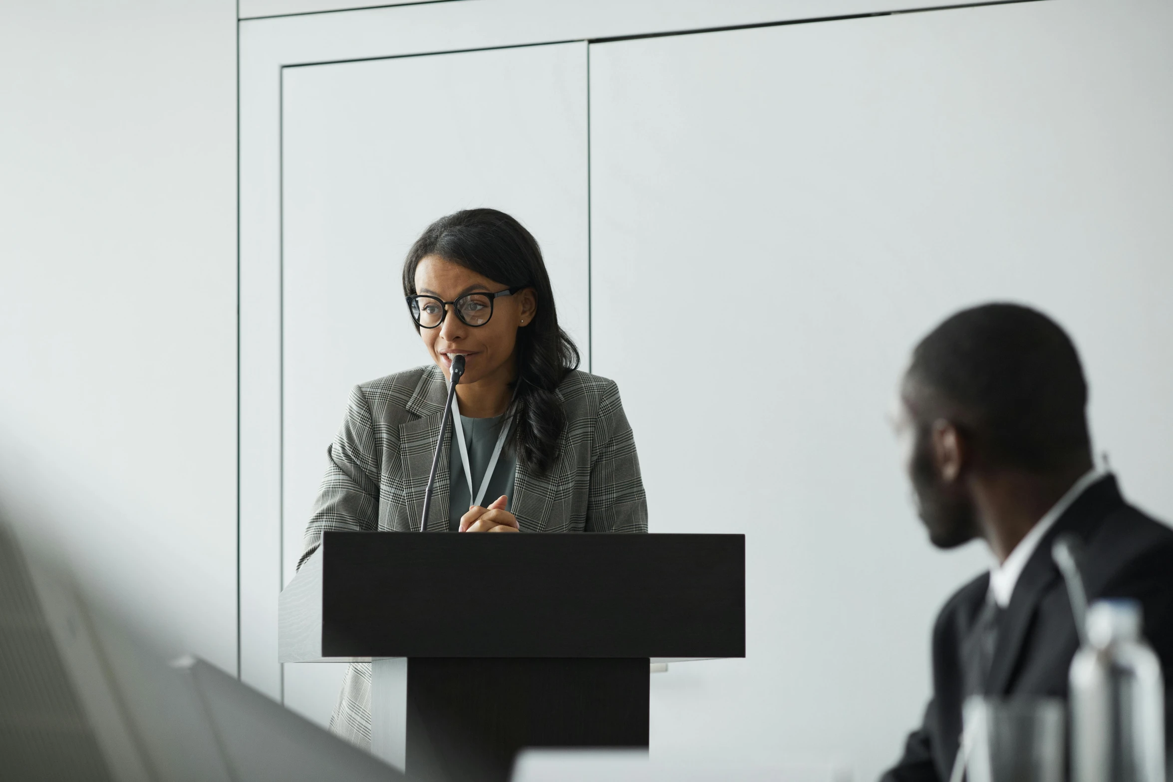 woman speaking at a podium with man in background