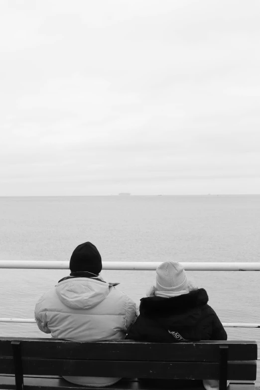 two people sitting on a bench near the ocean