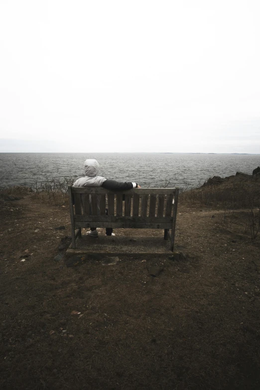 the woman sits on the bench overlooking the water