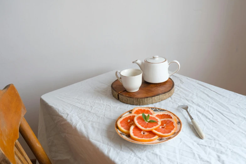 a plate with slices of oranges is sitting next to cups on a table