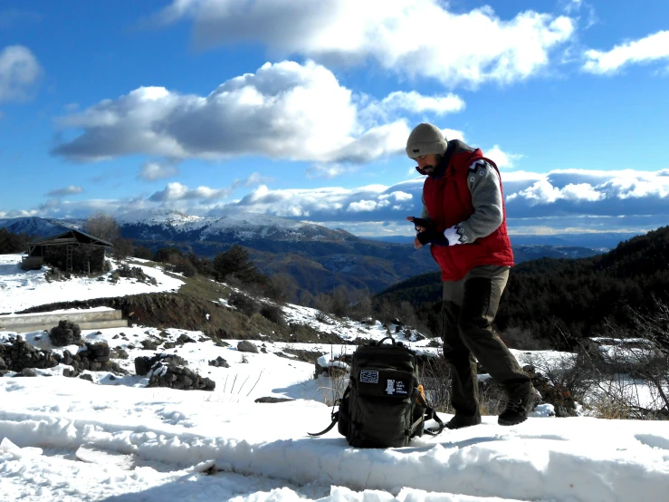 man standing in snowy terrain looking at his cellphone