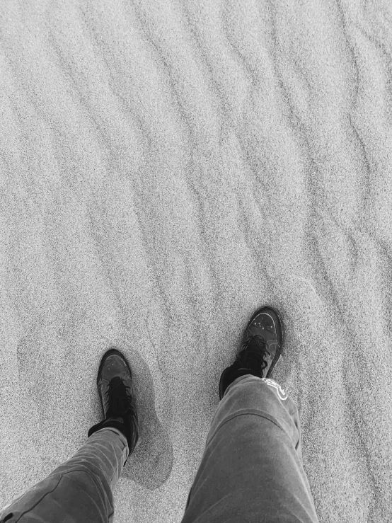 someone wearing black shoes standing in the sand