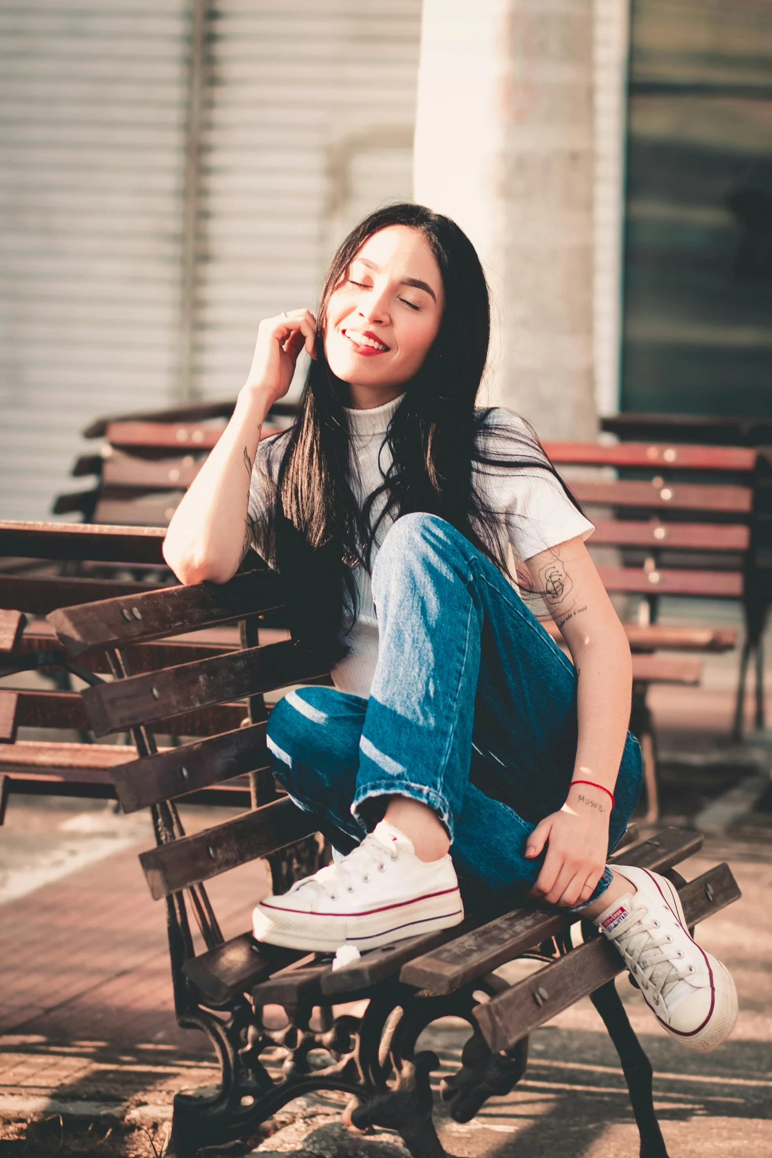 a woman in jean pants and sneakers sitting on a bench