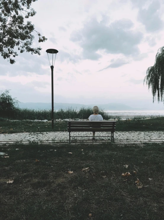 two people sit on a bench facing the ocean