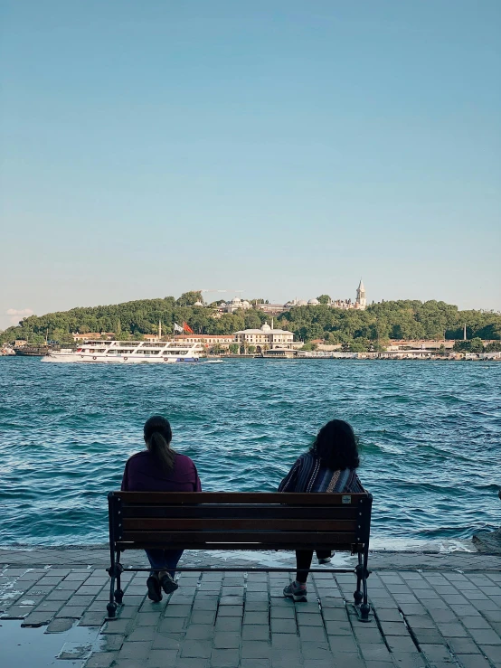 a couple of people sitting on a bench by the ocean