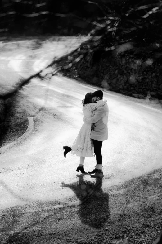 two people hugging on a road near some trees