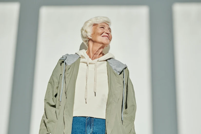 an older woman stands smiling on a light grey surface