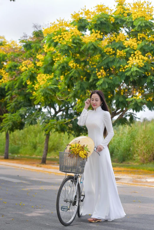 a girl in white is standing next to a bicycle and eating a fruit